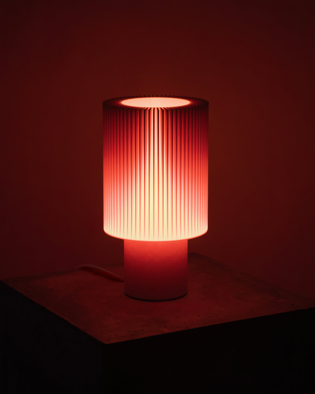 Lampe Iris Colors – Oxyde allumée, diffusant une lumière rougeoyante intense à travers un abat-jour nervuré, atmosphère vibrante et enveloppante.