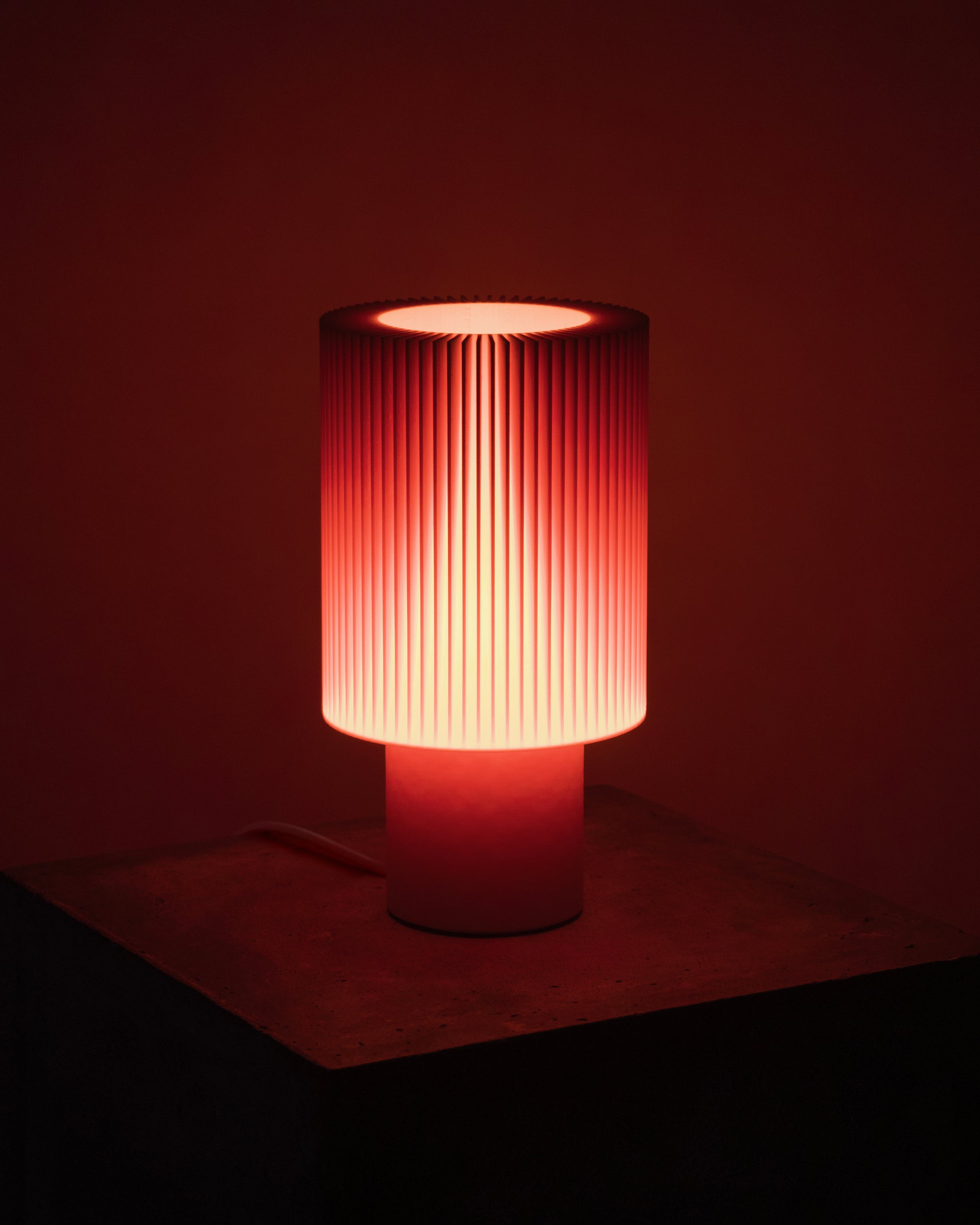 Lampe Iris Colors – Oxyde allumée, diffusant une lumière rougeoyante intense à travers un abat-jour nervuré, atmosphère vibrante et enveloppante.