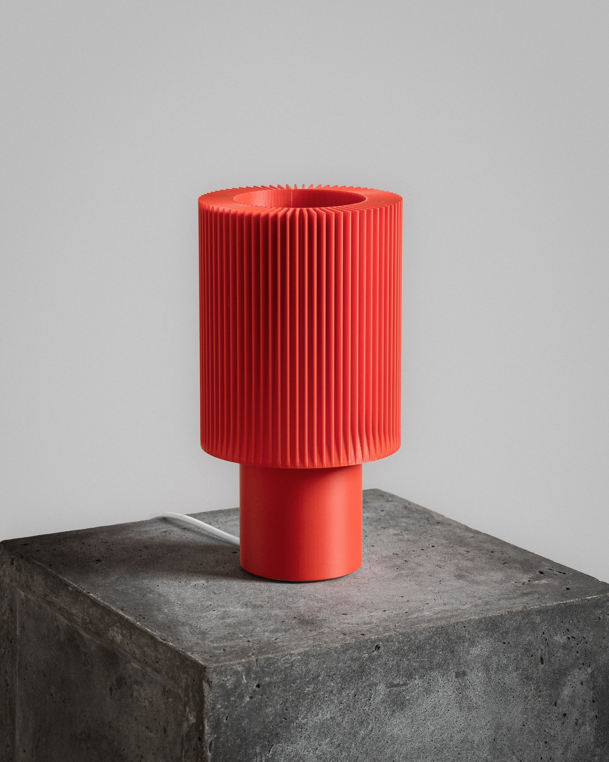 Lampe Iris Colors – Oxyde éteinte, imprimée en 3D, posée sur un socle en béton brut, rouge profond au design nervuré et sculptural.